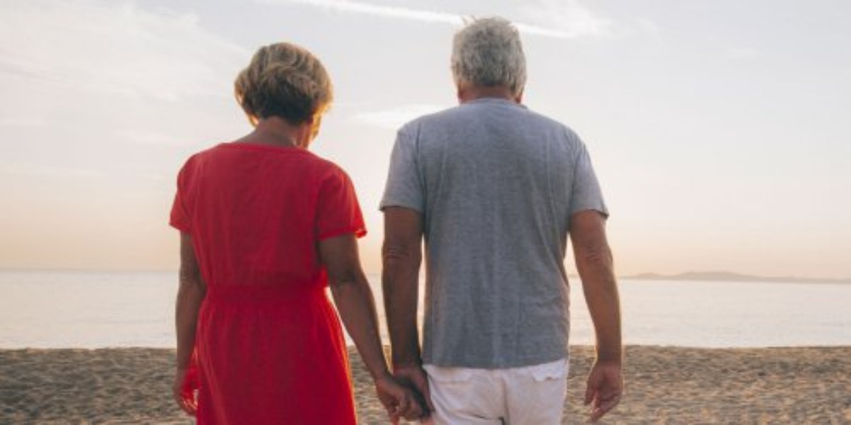 Couple marié marchant main dans la main sur la plage au coucher du soleil, symbole de 38 ans de mariage et des noces de mercure, représentant un amour durable, fluide et lumineux.